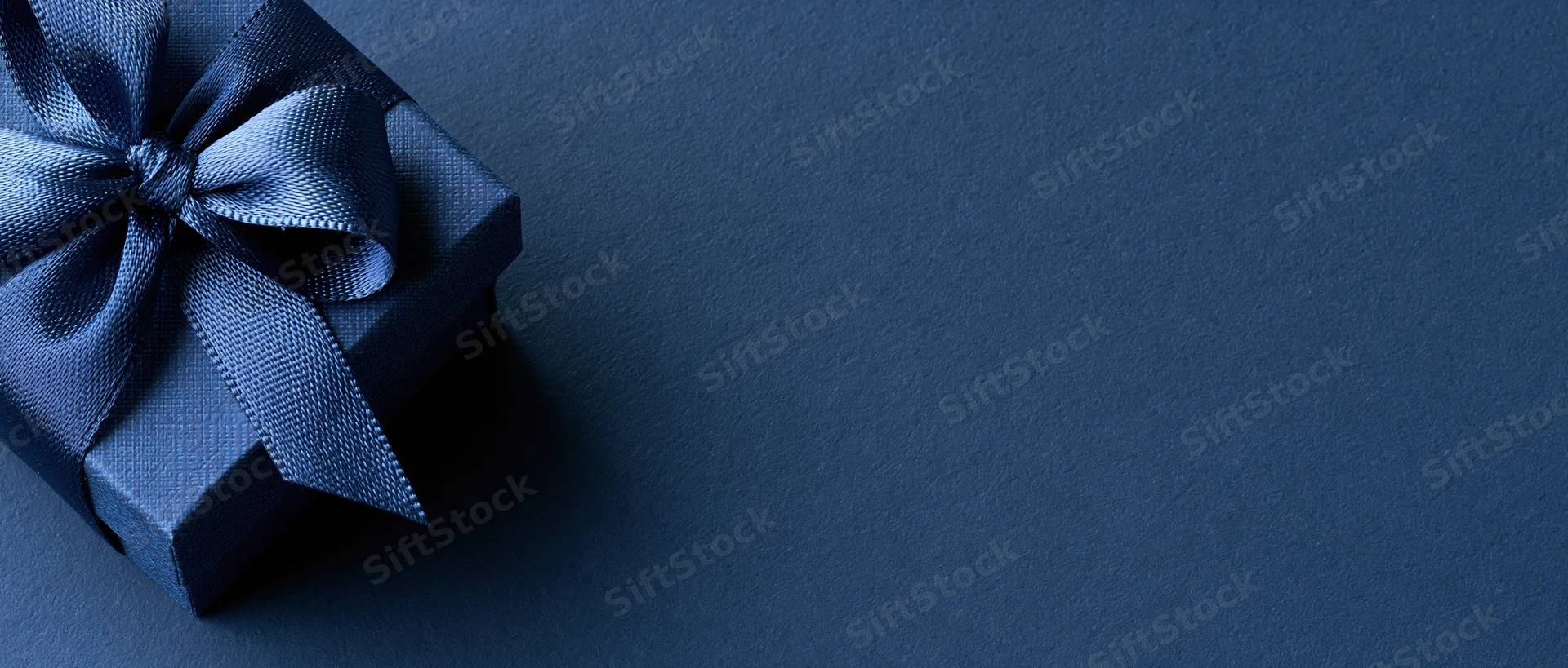 Navy blue gift box with satin ribbon bow on textured dark surface