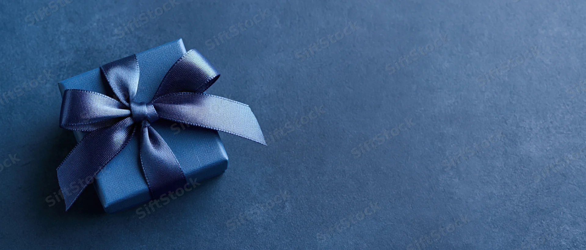Small navy blue gift box with satin ribbon bow on textured surface