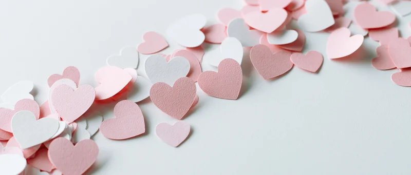 Paper heart confetti scattered across a clean white surface with copyspace