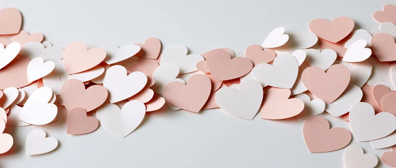 Scattered paper heart confetti in pink and white on a clean white surface