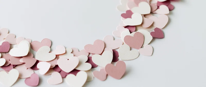 Scattered paper heart confetti in soft pink and white tones on a white surface