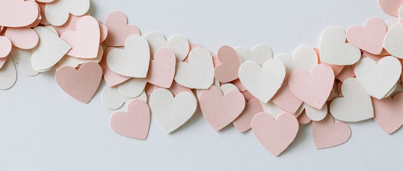 Scattered paper heart confetti in a loose arc on white surface