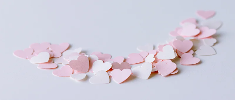 Paper heart confetti scattered in a loose arc on a white surface