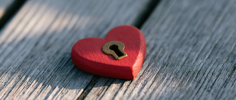 Red wooden heart with brass keyhole resting on weathered wooden surface