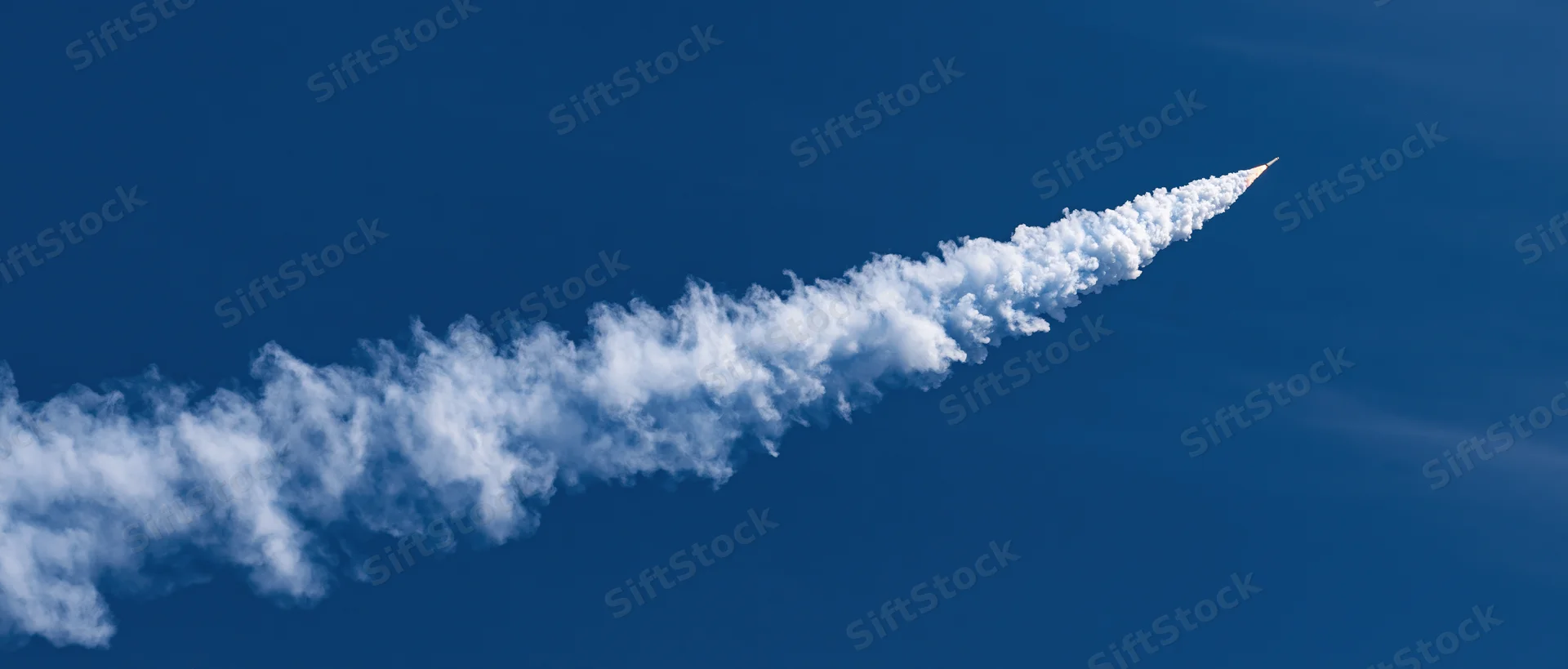 Rocket launching upward leaving a white smoke trail across deep blue sky