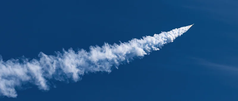 Rocket launching upward leaving a white smoke trail across deep blue sky