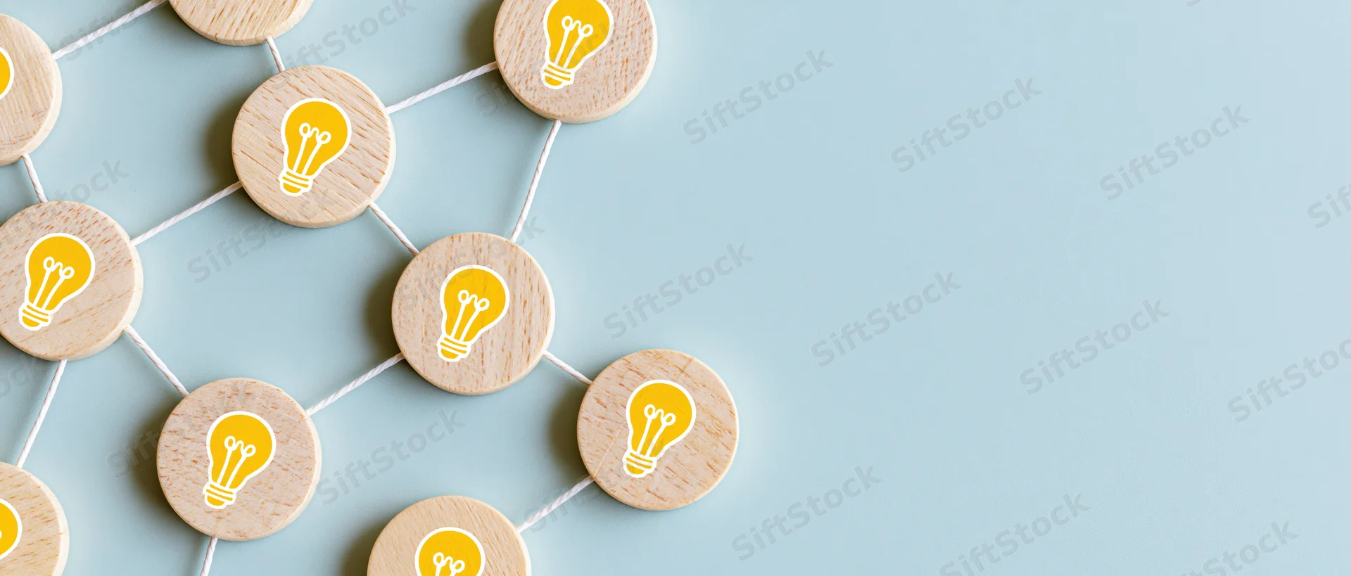 Wooden tokens with yellow lightbulb icons connected by string in a network pattern on light blue surface
