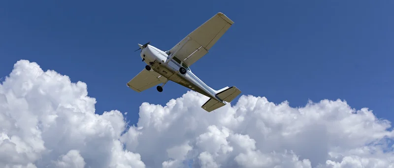 Small white single-engine propeller plane flying overhead against blue sky with white clouds