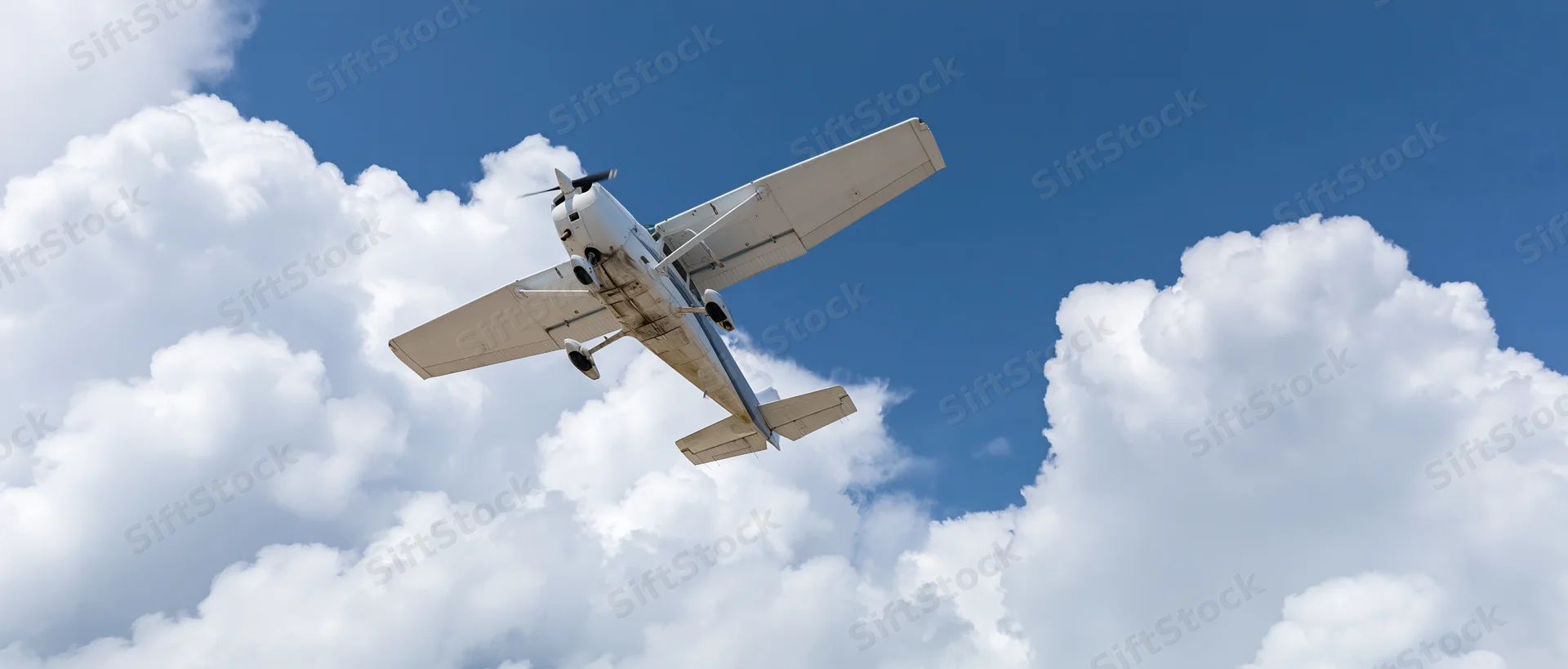Small white single-engine propeller plane flying overhead against blue sky with white clouds