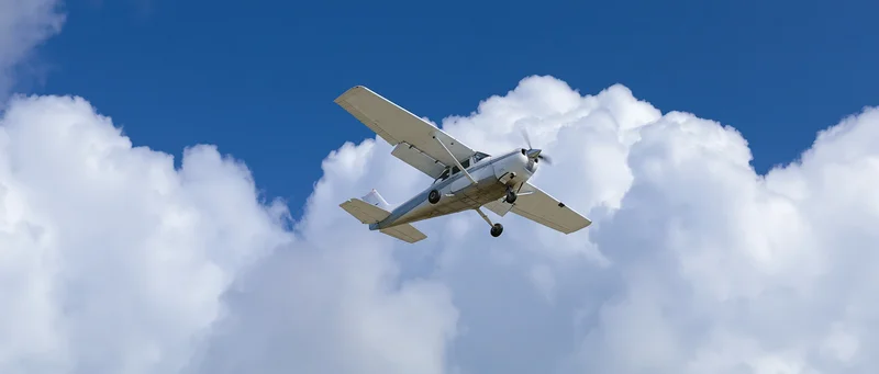 Small white single-engine propeller plane flying overhead against blue sky with white clouds