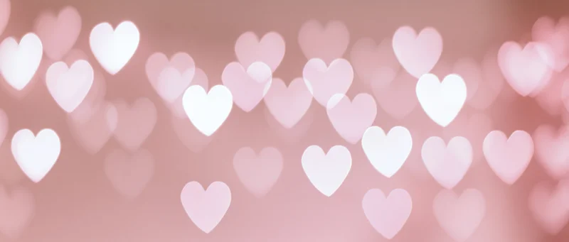 Soft pink bokeh background with out-of-focus heart shapes floating across the frame