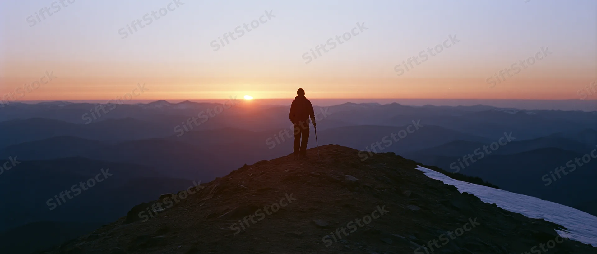 Hiker standing on mountain peak at sunset holding trekking pole