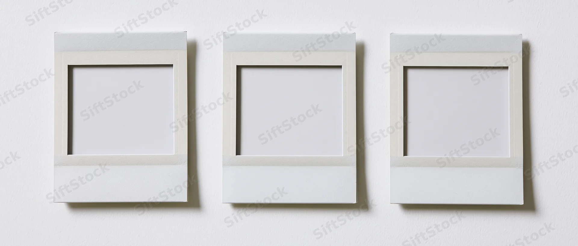 Three blank instant photo prints arranged side by side on a white wall