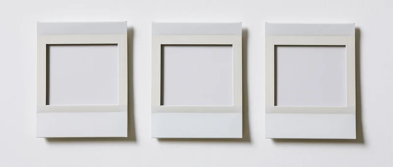 Three blank instant photo prints arranged side by side on a white wall