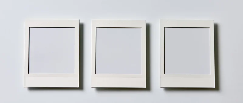 Three blank instant photo prints arranged side by side on a white wall