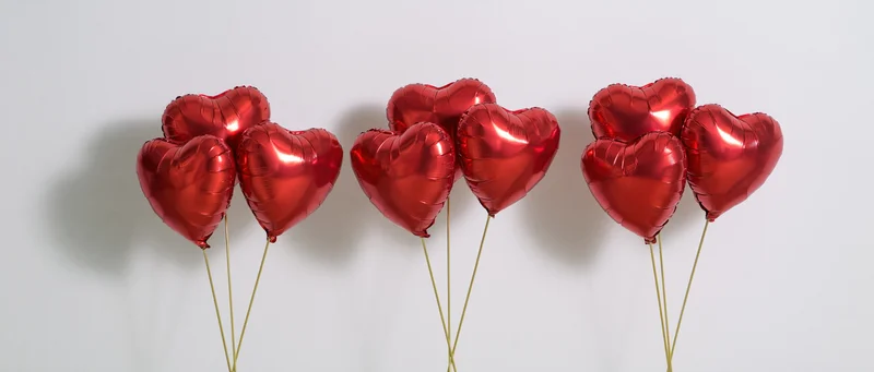 Three clusters of red metallic heart-shaped balloons arranged in a row against a white background