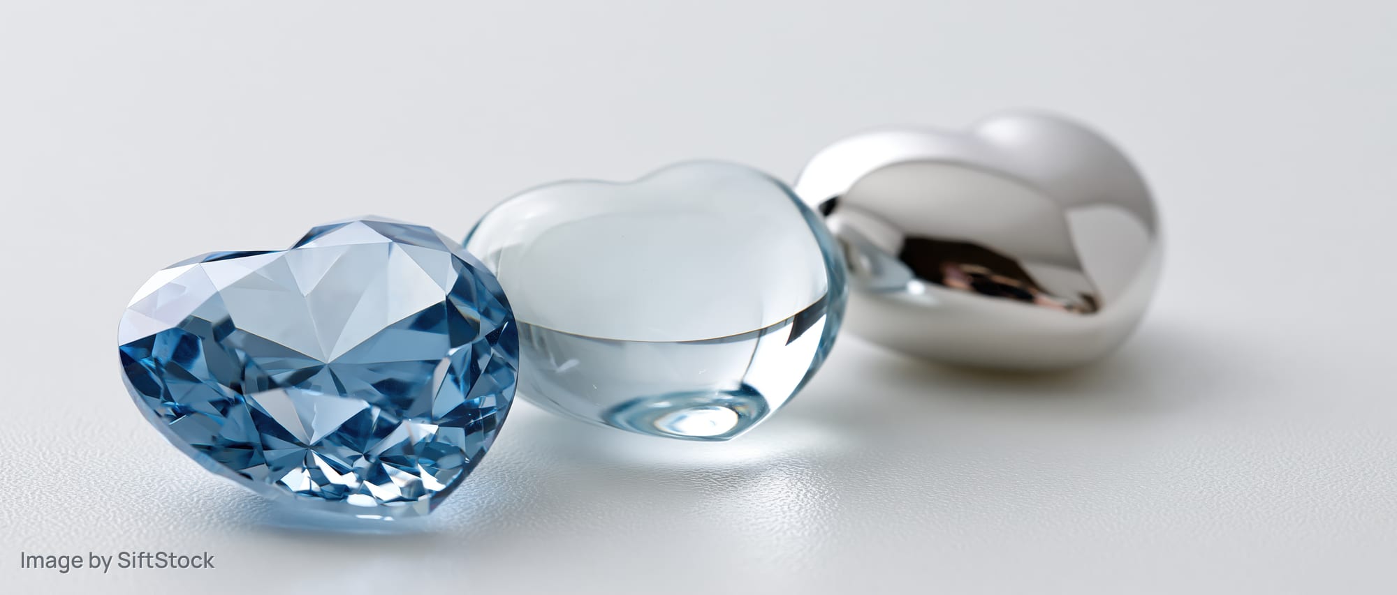 Three heart-shaped gemstones and metal objects arranged in a row on a white surface