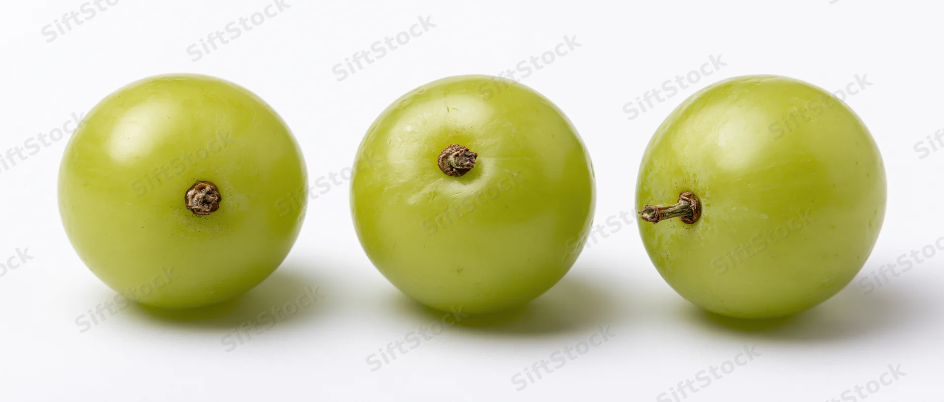 Three green grapes in a row on a white surface