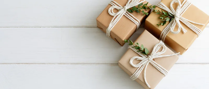 Three kraft paper gift boxes tied with white twine bows arranged on a white wooden table with copyspace
