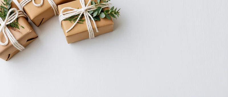 Three kraft paper gift boxes tied with white twine bows and eucalyptus sprigs arranged on a white surface