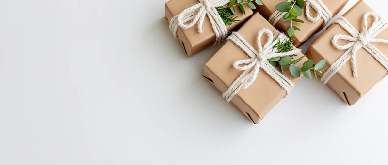 Three kraft paper gift boxes tied with white twine bows and eucalyptus sprigs arranged on white surface
