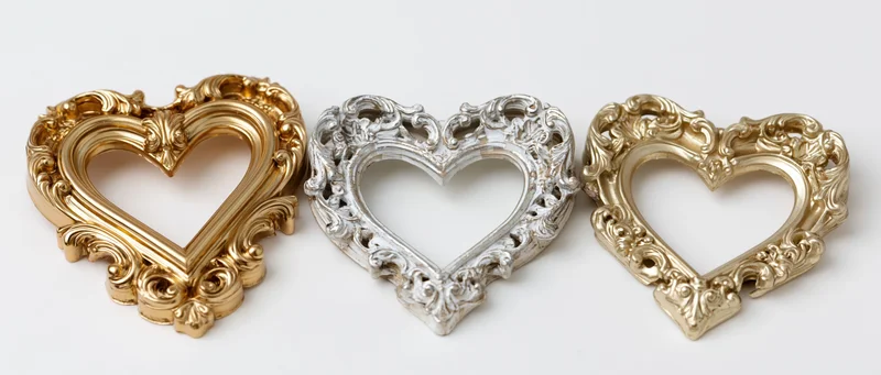 Three ornate heart-shaped frames in gold, silver, and champagne tones arranged side by side on a white background