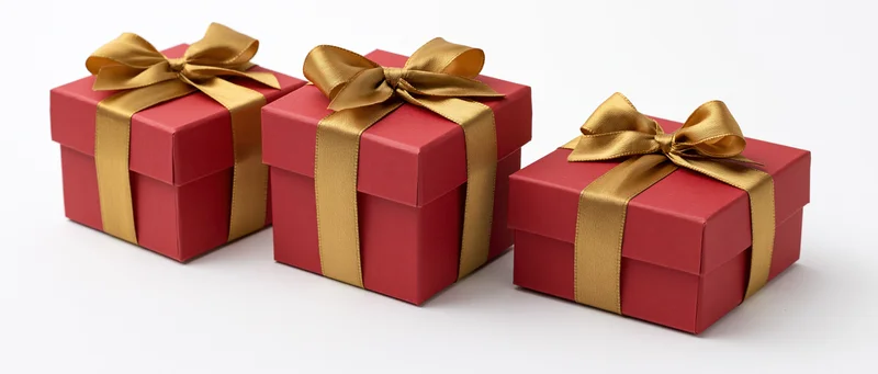 Three red gift boxes with gold satin ribbons and bows arranged in a row on a white surface