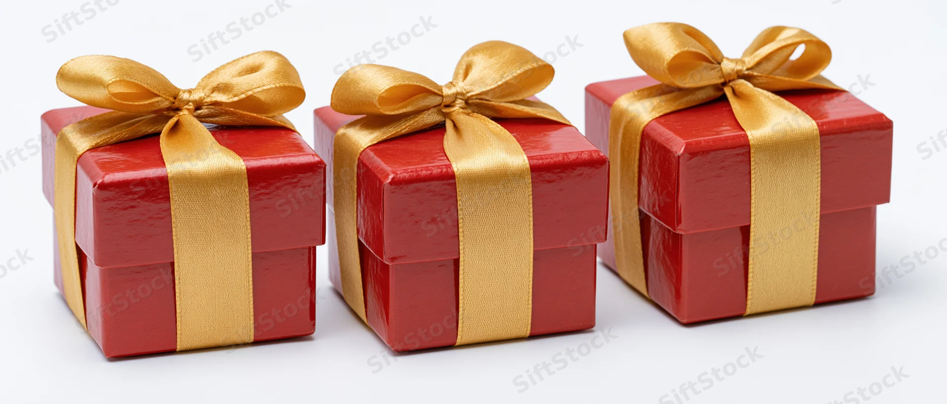 Three red gift boxes with gold satin ribbons and bows arranged in a row on white background
