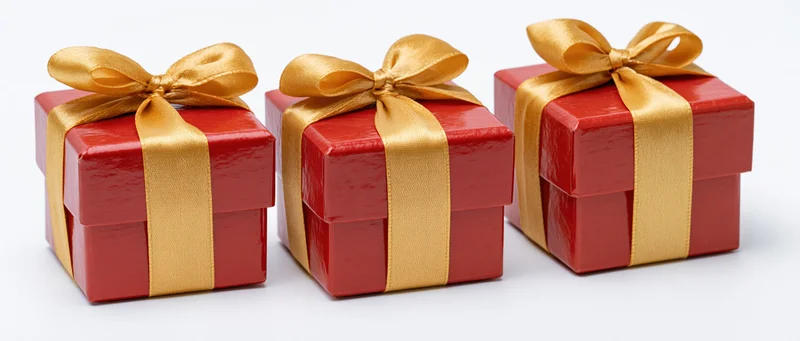 Three red gift boxes with gold satin ribbons and bows arranged in a row on white background