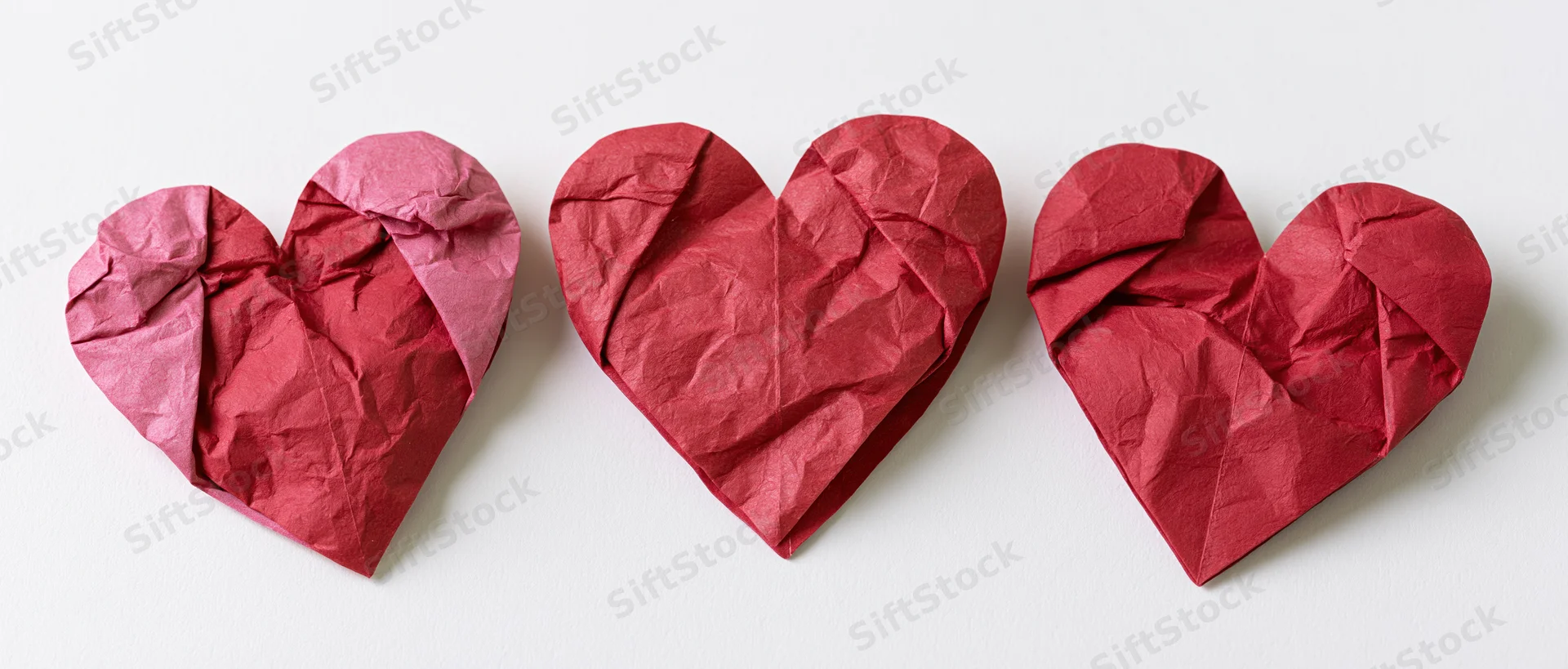 Three red paper hearts arranged in a row on white background