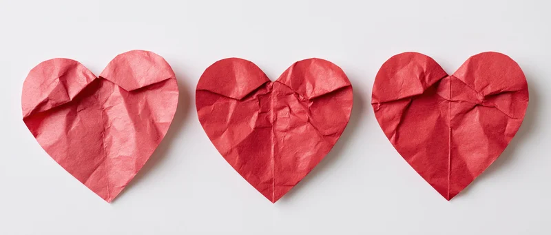 Three red crumpled paper hearts arranged in a row on white background