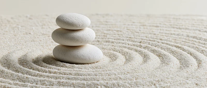 Three white stones stacked in a balanced tower on raked sand with concentric circles