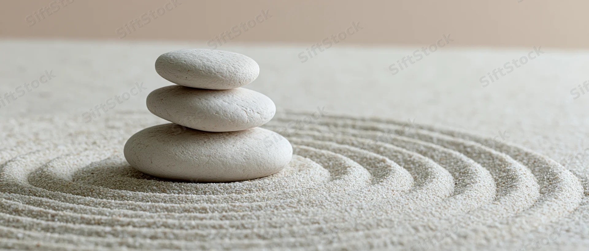 Three white smooth stones stacked in a balanced tower on raked sand with concentric patterns