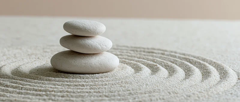 Three white smooth stones stacked in a balanced tower on raked sand with concentric patterns
