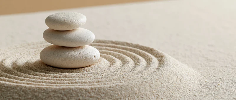 Three white stones stacked in a balanced tower on raked sand with circular patterns