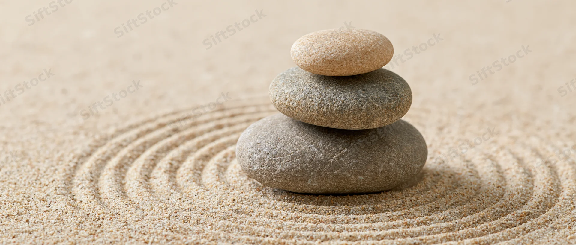 Three smooth stones stacked in a balanced cairn on raked sand with concentric circles