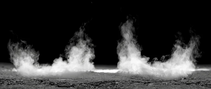 White smoke rising in columns from rough ground against black background