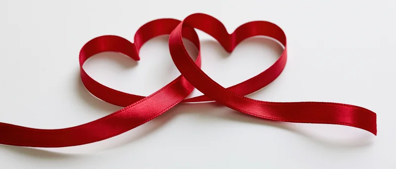 Two interlinked heart shapes formed from a single red satin ribbon on white background