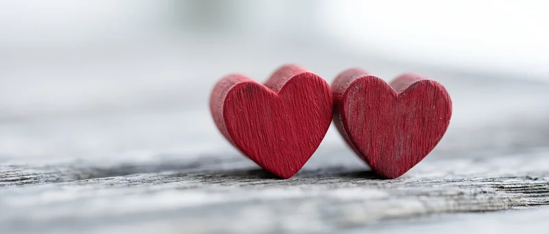 Two red wooden heart figurines resting side by side on a weathered gray surface
