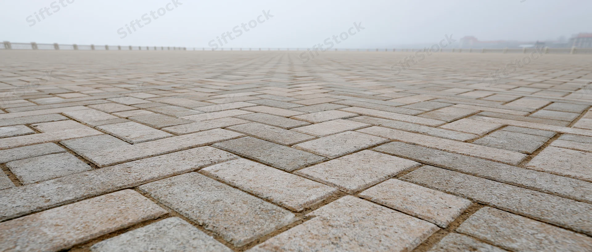 Wide-angle view of a herringbone-patterned concrete brick pavement in an empty public plaza under overcast sky