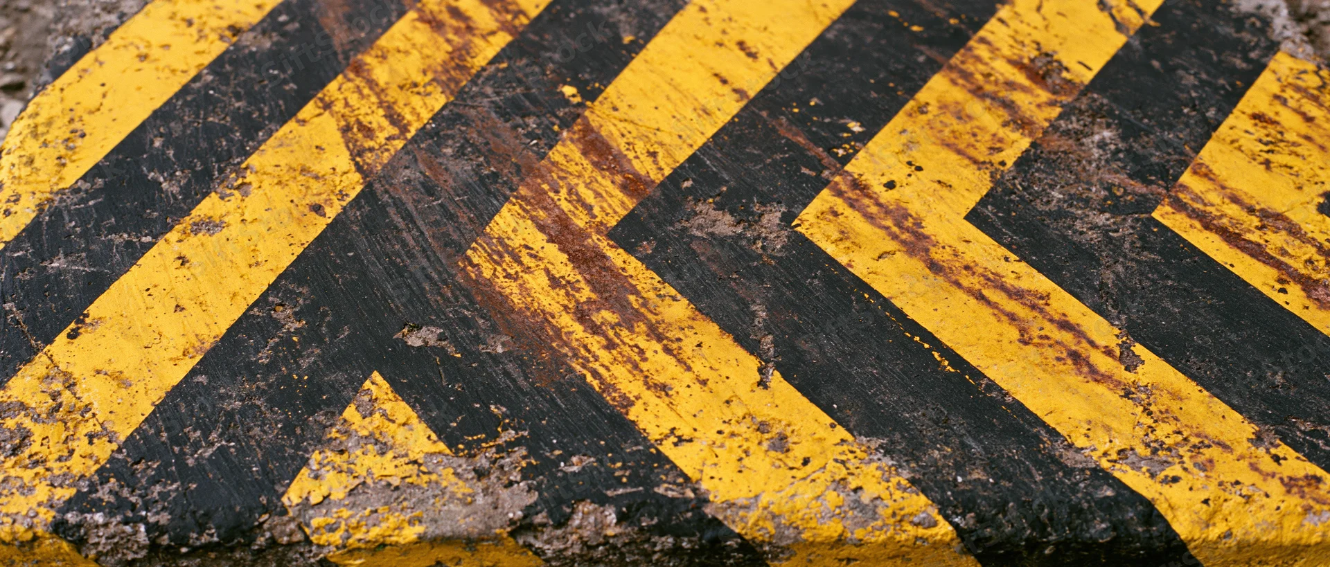 Weathered industrial warning barrier surface with diagonal yellow and black stripes showing rust and paint wear