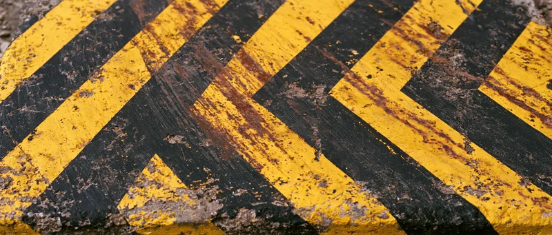 Weathered industrial warning barrier surface with diagonal yellow and black stripes showing rust and paint wear