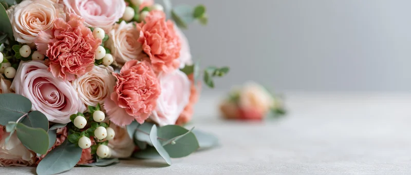 Wedding bouquet of pink roses and coral carnations with white berries and eucalyptus on a light surface