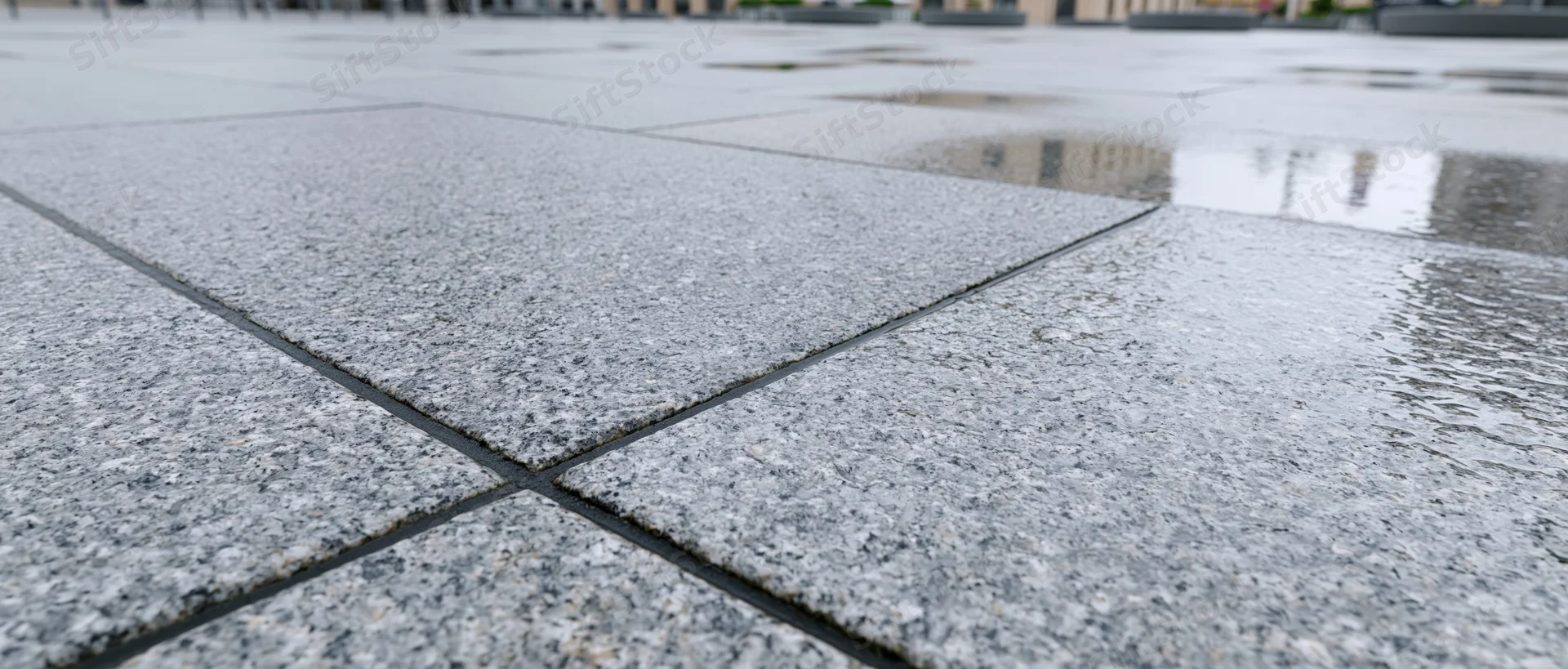 Wet granite paving stones on an empty outdoor plaza with puddles reflecting buildings