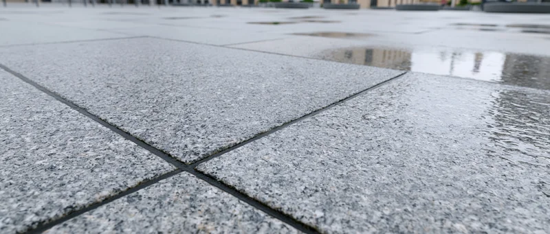 Wet granite paving stones on an empty outdoor plaza with puddles reflecting buildings