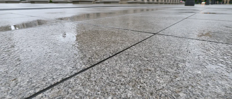 Wet granite paving stones on an empty outdoor plaza with reflections and grout lines