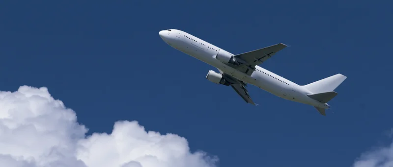 White commercial passenger jet climbing in blue sky with clouds below