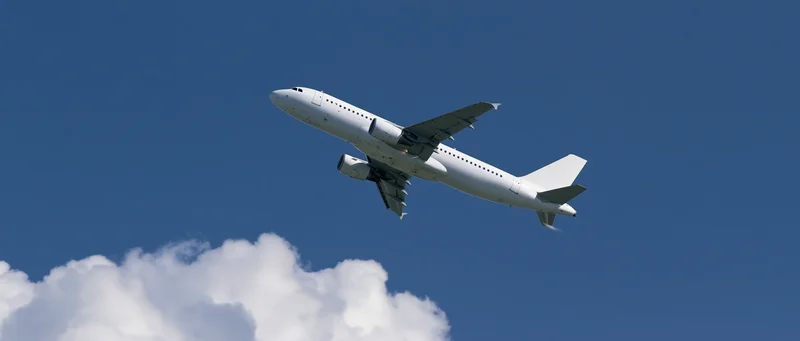 White commercial passenger jet climbing in blue sky above clouds