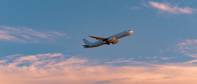 White commercial passenger jet climbing through open sky at sunset