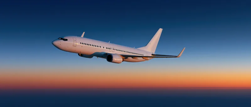 White commercial passenger jet flying at cruise altitude against a twilight sky gradient